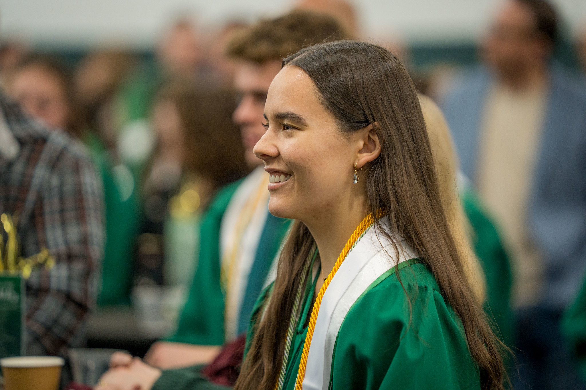 Image of Honors College graduate Sloane Barlow in a green graduation gown, white Honors stole, and cords, smiling.