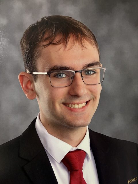 Professional image of incoming MSU Honors College student and Williams Scholar Luke Compton smiling in a black suit jacket, white collared shirt, and red tie against a grey gradient background.