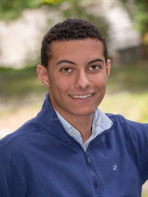 Image of incoming MSU Honors College student and Williams Scholar Brady Crossetta smiling in a navy quarter-zip and blue collared shirt. Blurred greenery is in the background.