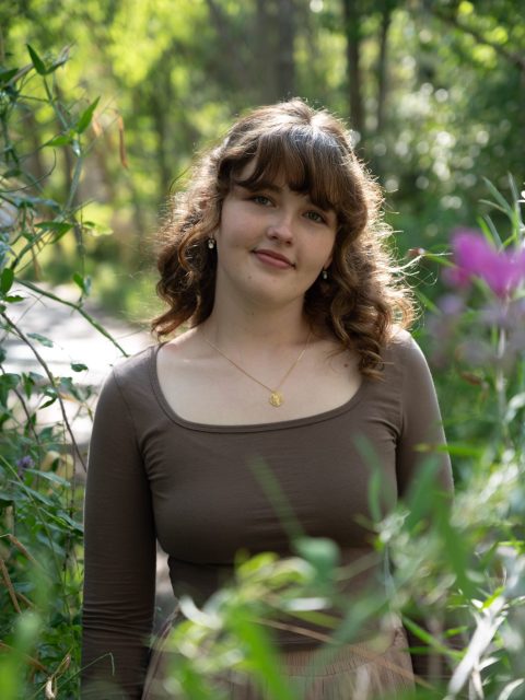 Image of incoming MSU Honors College student and Williams Scholar Aletha Elser standing in a wooded area in a brown long-sleeve shirt.