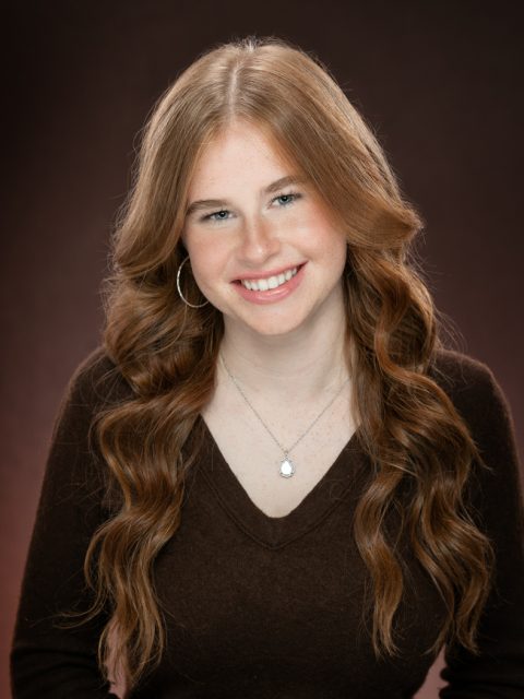 Professional image of incoming MSU Honors College student and Williams Scholar Anna Foote smiling in a dark brown top against a glowing brown background.