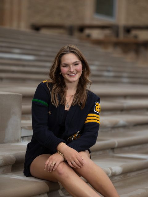 Image of incoming MSU Honors College student and Williams Scholar Mia Juzych sitting and smiling on large steps outside a building. Juzych is wearing an oversized navy cardigan.