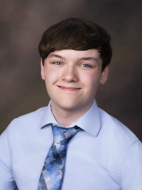 Professional image of incoming MSU Honors College student and Williams Scholar Paul Krone softly smiling in a blue collared shirt and colorful necktie against a dark gradient background.
