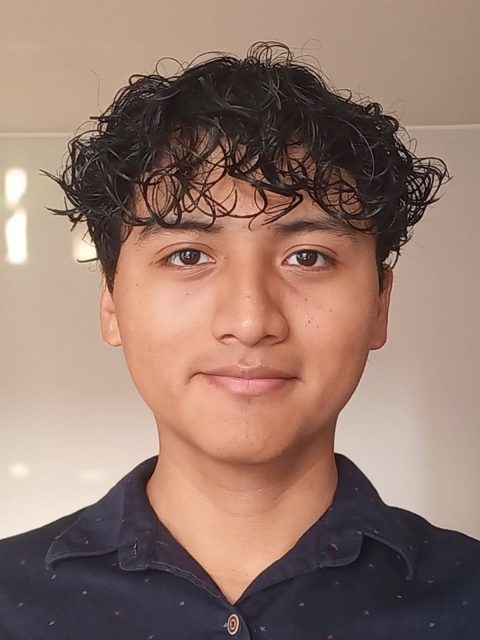 Image of incoming MSU Honors College student and Williams Scholar David Rivera Lopez wearing a dark collared shirt. A whiteboard and tan wall are in the background.