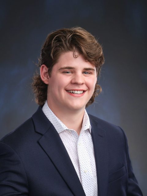 Prodessional image of incoming MSU Honors College student and Williams Scholar Ben Rolain smiling in a dark suit jacket and white collared shirt against a dark gradient background.