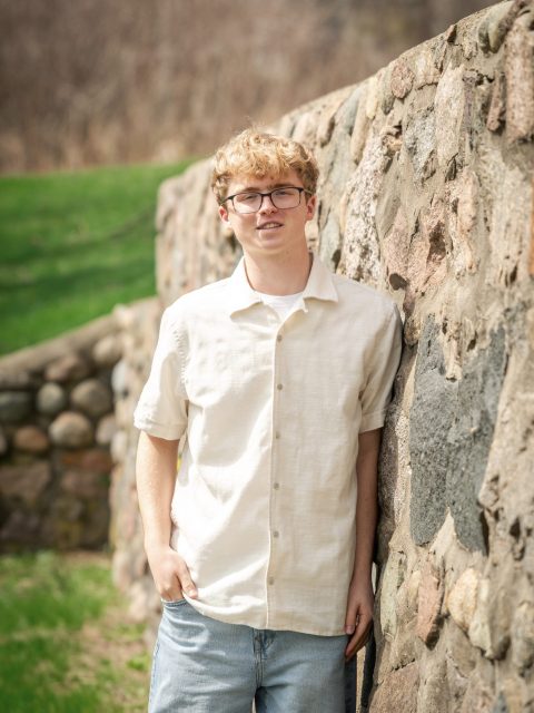 Image of incoming MSU Honors College student and Williams Scholar Isaac Thomas leaning against a stone wall in a white collared shirt and blue jeans.