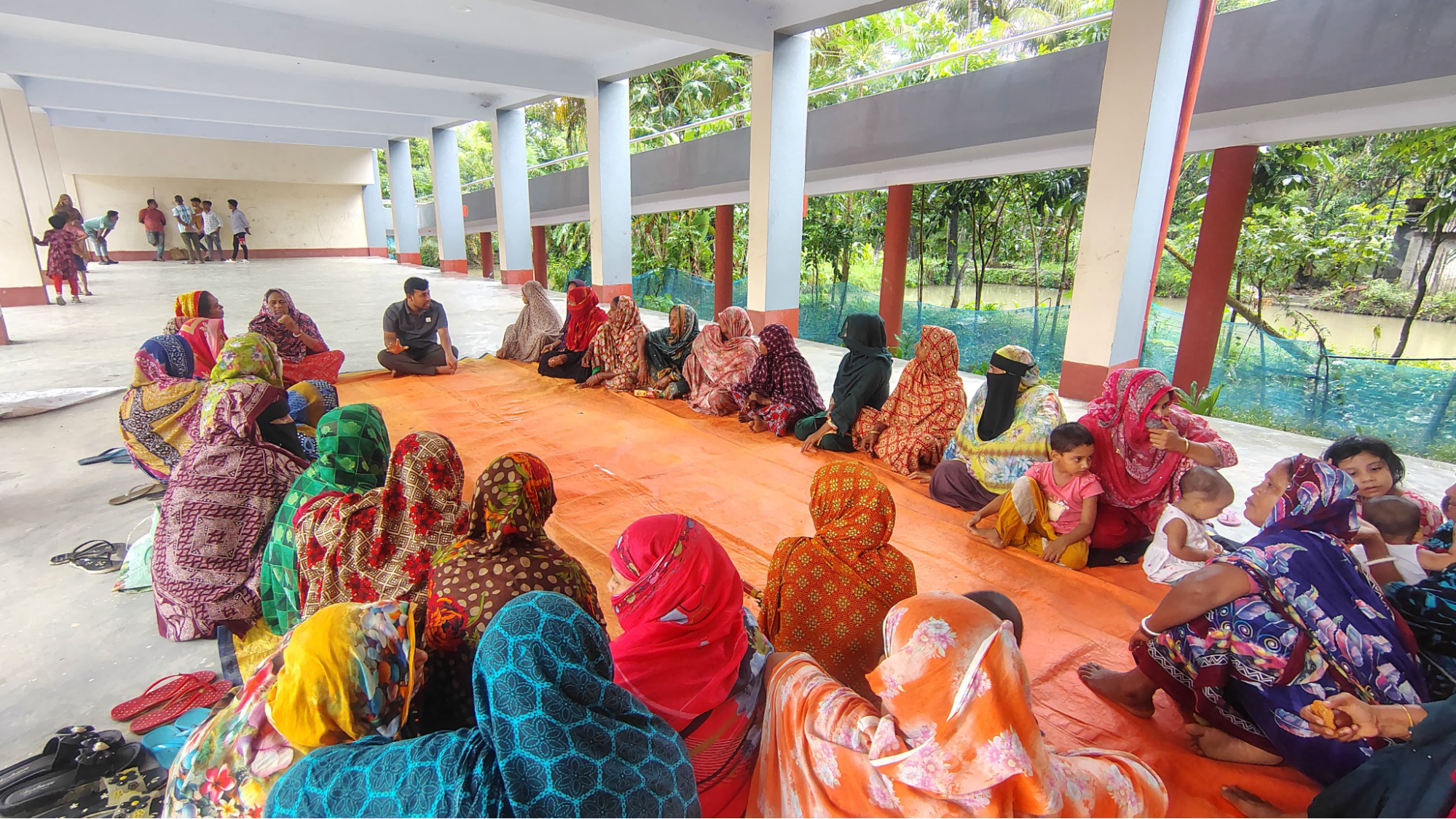 Gobindapur residents seated around a large orange tarp for a community meeting on safe water use, maintenance and the importance of clean water.