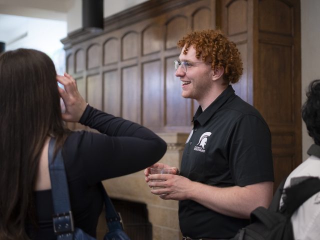 Honors College student Jagger Wraalstad conversing with others in the Schupbach Van Wagenen Fireside Lounge inside Campbell Hall.