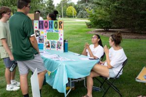 Photo of Honors Times Two leaders talking to student at the Honors College Resource Fair. They sit at a decorated table with a trifold detailing their club.