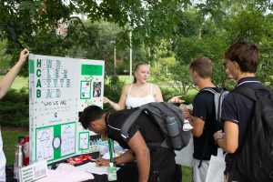 Photo of student standing in front of HCAB club sign at the Honors College Resource Fair explaining their club to another student.