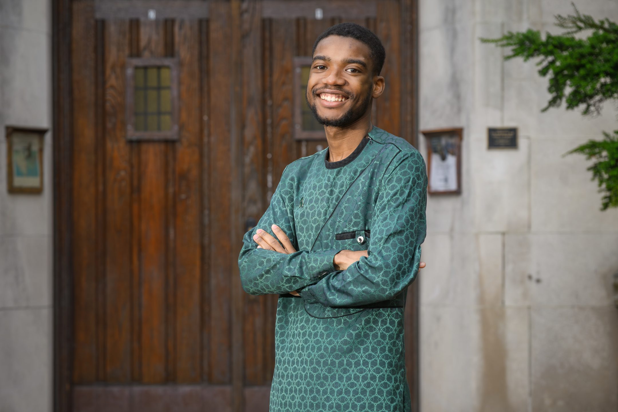 Honors College student Benjamin Nketsiah standing and smiling in front of Beaumont Tower with arms folded, wearing a green long-sleeved shirt.