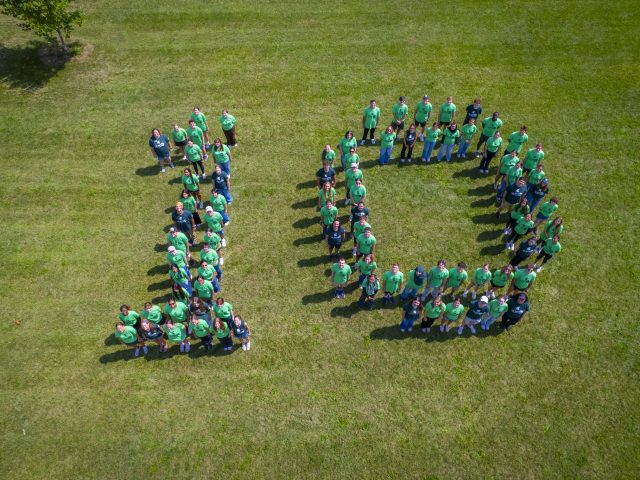 Aerial view of Honors College students, staff, and program partners for HC IMPACT arranged in the number 10. They are all wearing program t-shirts in various shades of green.