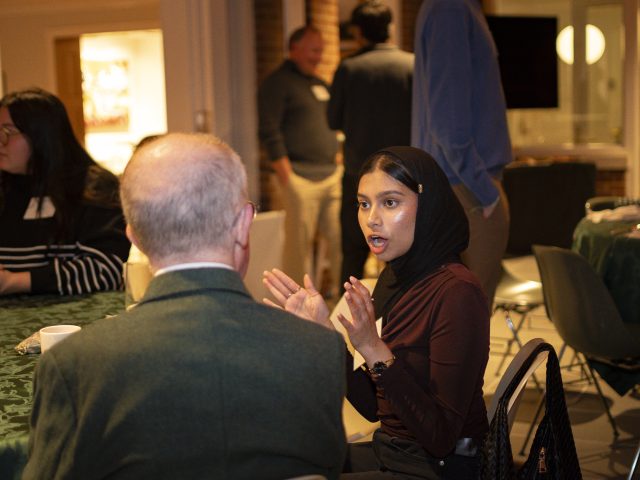 MSU Honors College student Sanaa Bashar talking with donor Bill Schoenl, while both are seated at a table for a scholarship dinner at Cowles House.
