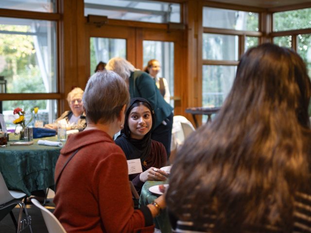 MSU Honors College student Sanaa Bashar smiling at donor Bill Schoenl, while both are seated at a table for a scholarship dinner at Cowles House.
