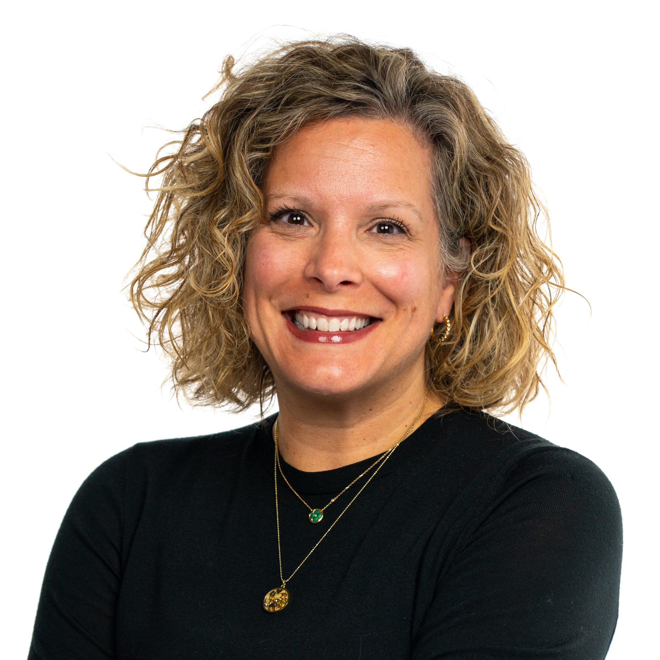 Michigan State University Honors College alumna Sara Dolan smiling in a black shirt and gold jewelry against a white background.